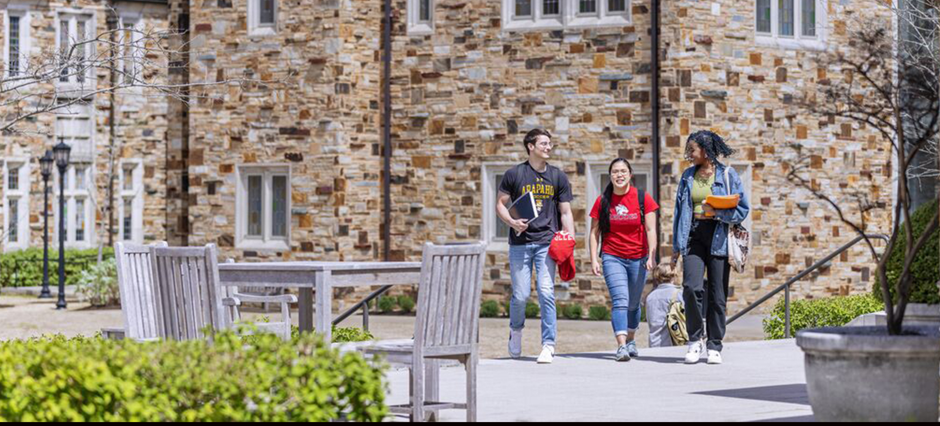 A group of three students on a spacious walkway with a two-story, collegiate gothic building in the background.