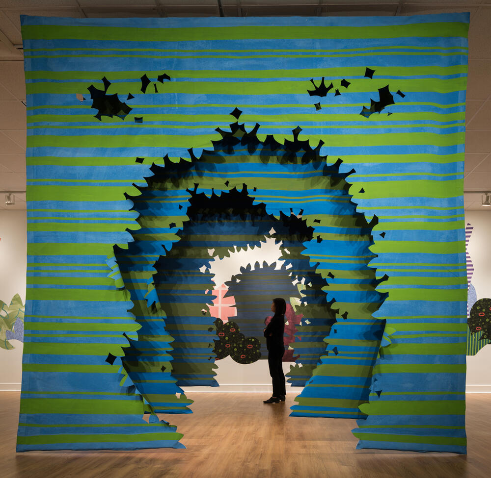 a person stands inside a large installation of cutouts of a tunnel of trees