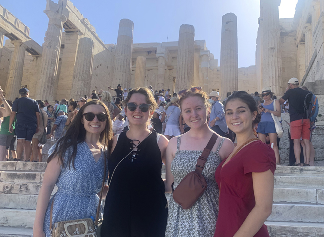 four young women pose in front of the Acropolis