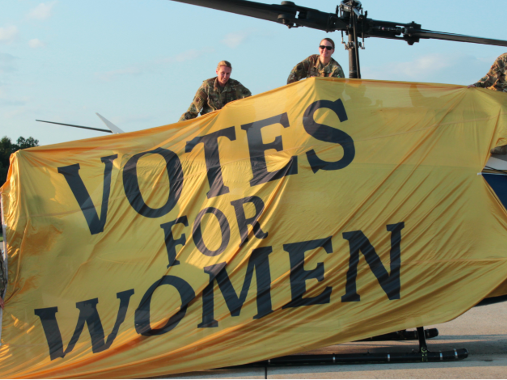 women in uniform hold up a banner 