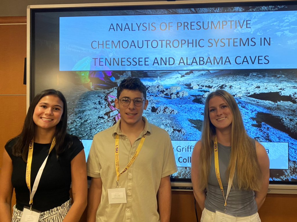 three Rhodes College students standing in front of a board displaying their research