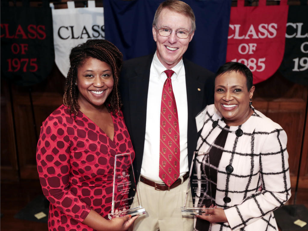 two african american women holding awards and hugging an older white male