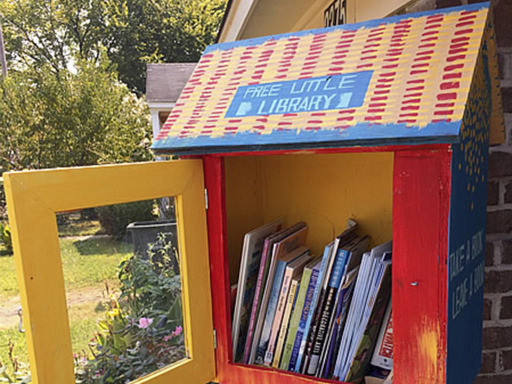 A quaint birdhouse painted in primary colors that has been repurposed to be a miniature library