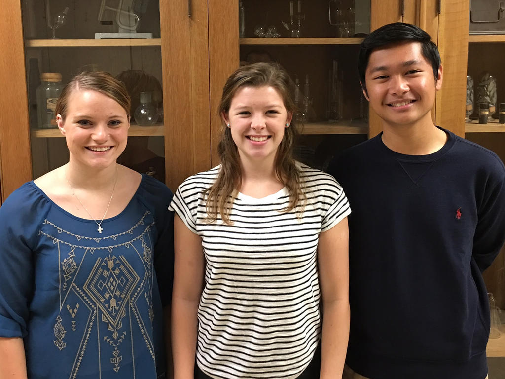 From left to right: a blonde female student wearing a slicked back ponytail and smiling, another blonde female student with a gray and white striped shirt, and an Asian male wearing a black t-shirt