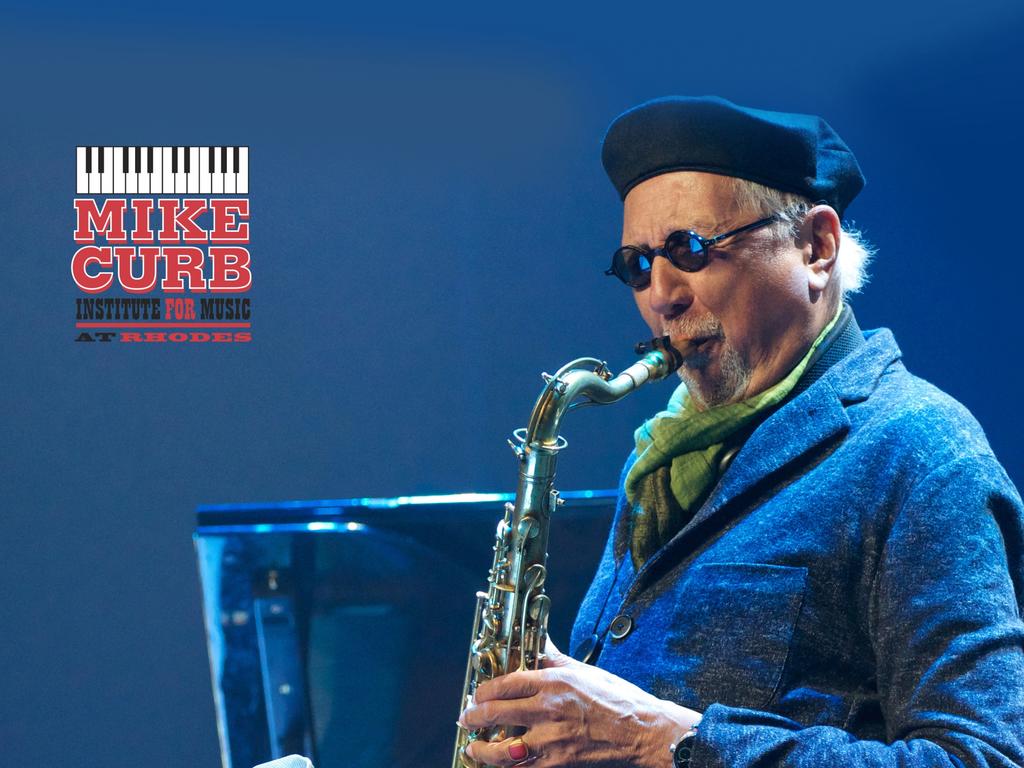 A man with a beret and sunglasses playing the saxophone on a blue-lit stage