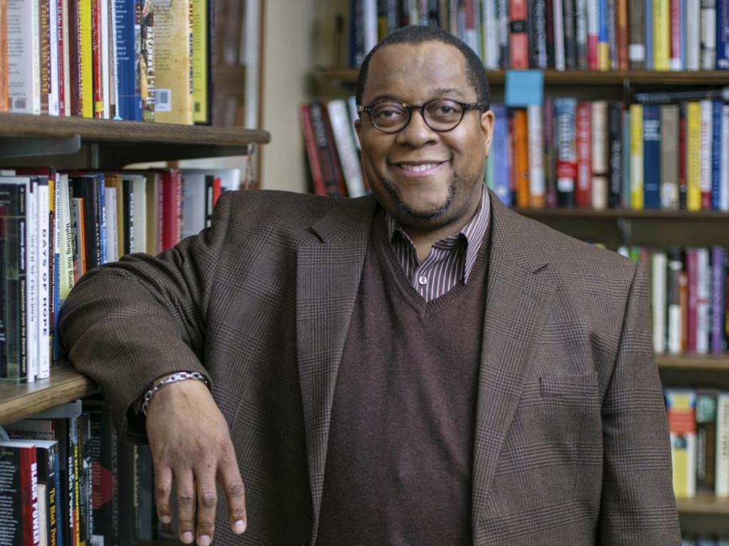 an African-American professor smiling and standing in front of a book shelf