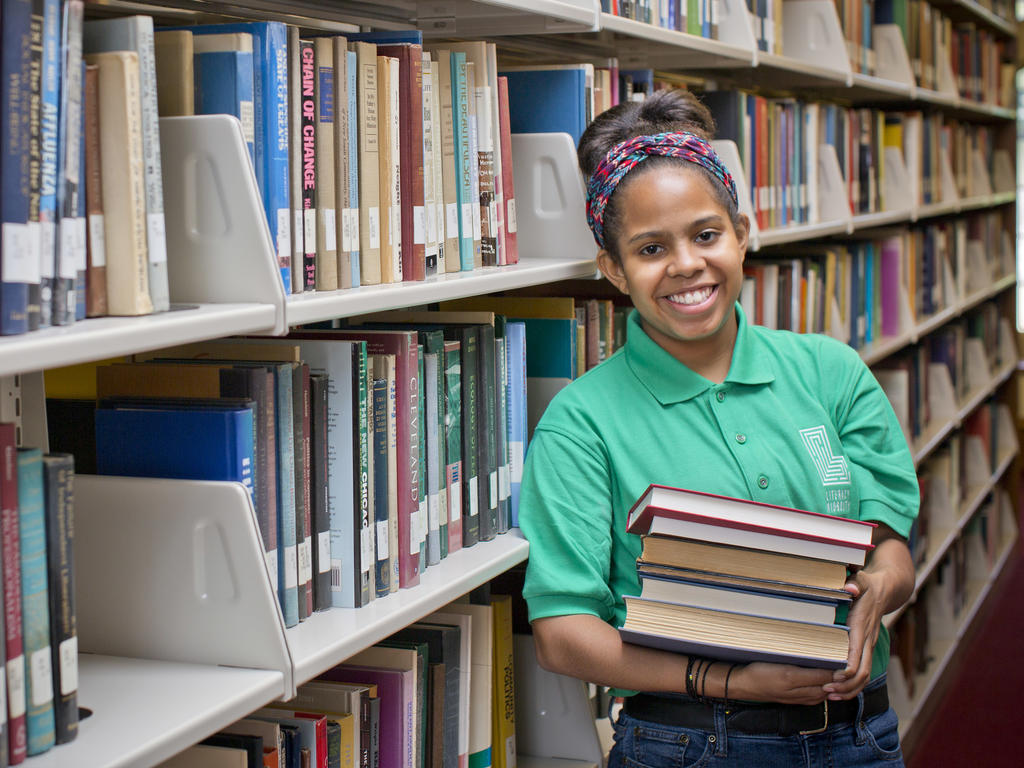 a young student standing in front of a large bookshelf 