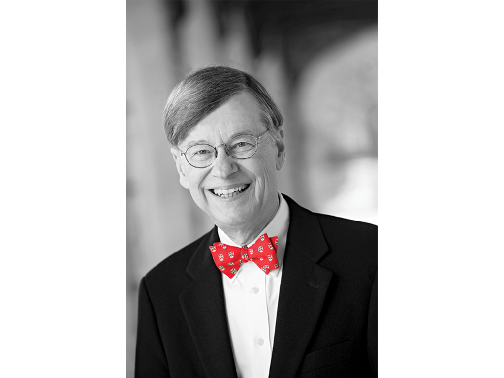 a black and white image of an old white male (the president of the college), with the only color being the red bow tie he is wearing