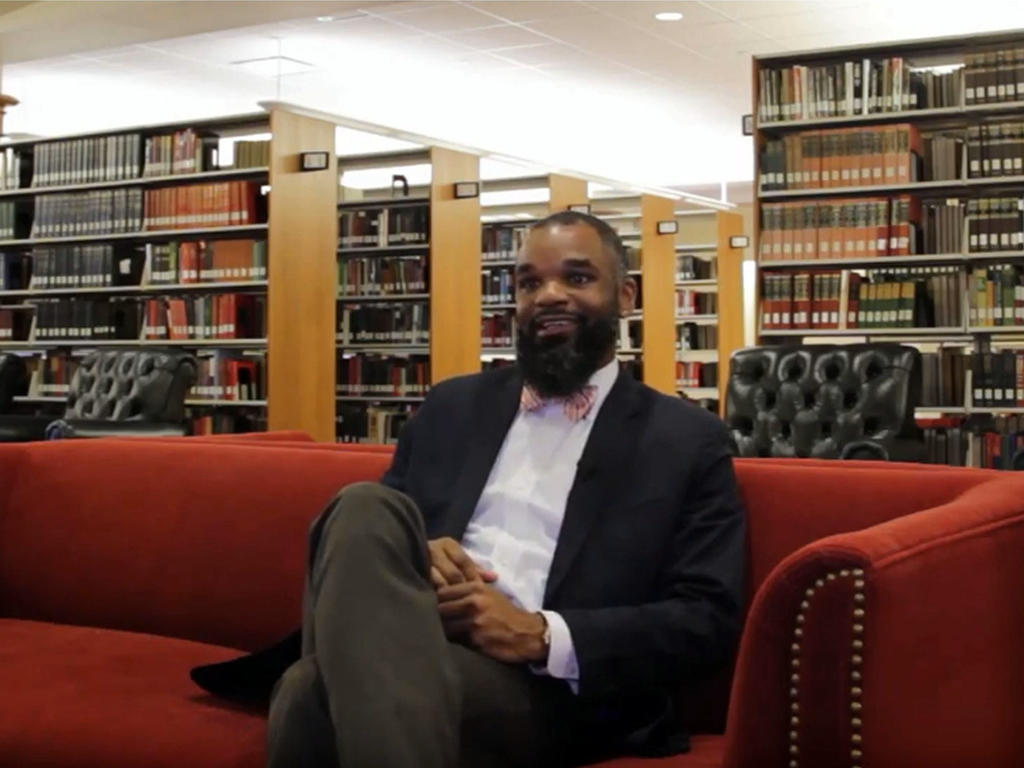 an African American professor sitting on a couch in the library