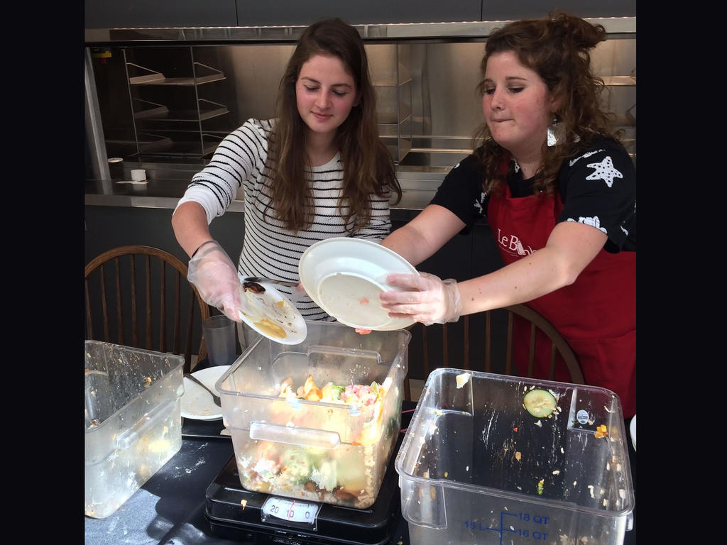 two students scooping leftover food into tubs