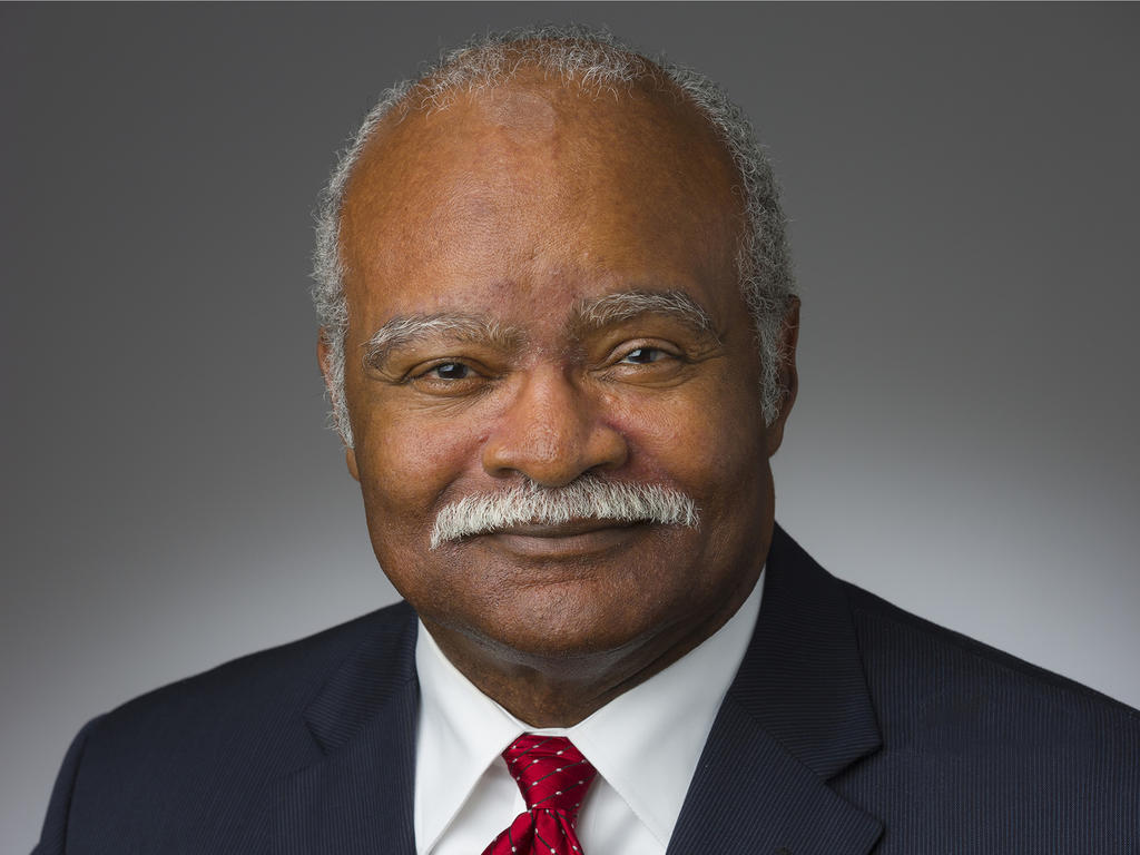 a headshot of an older, African American man in front of a grey background