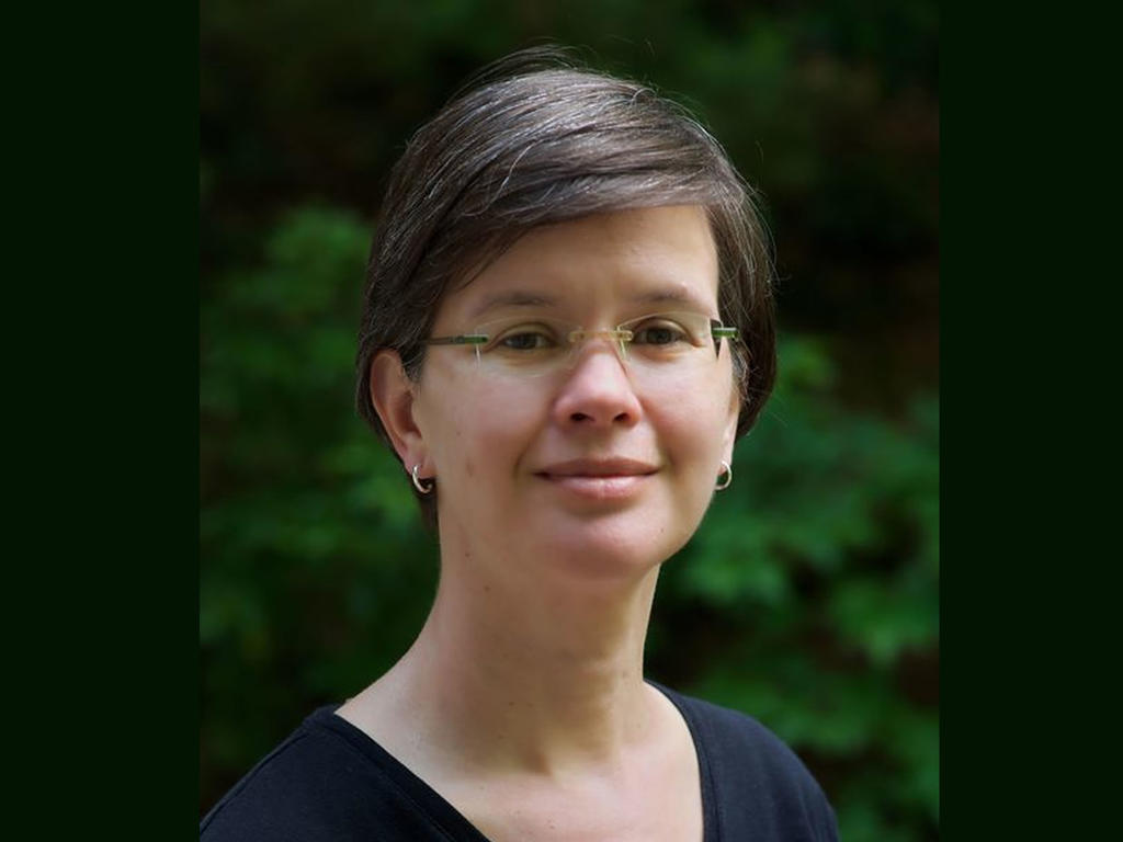 a headshot of a middle aged female professor in front of shrubbery