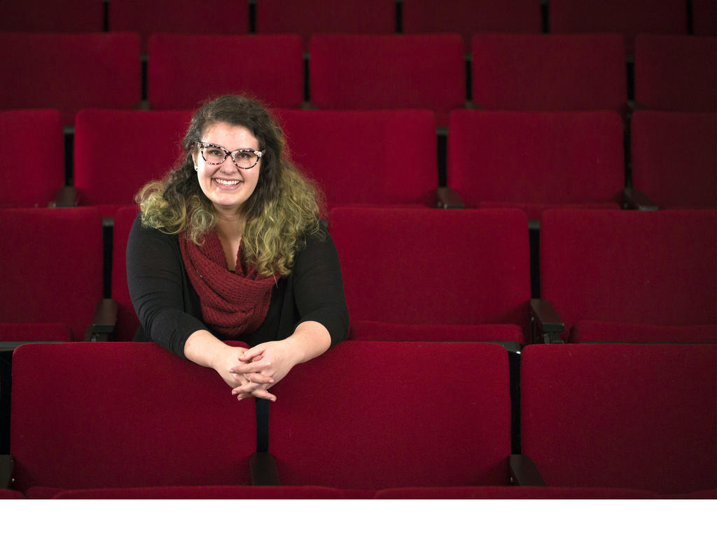 a young white woman seating casually amongst red theatre seats