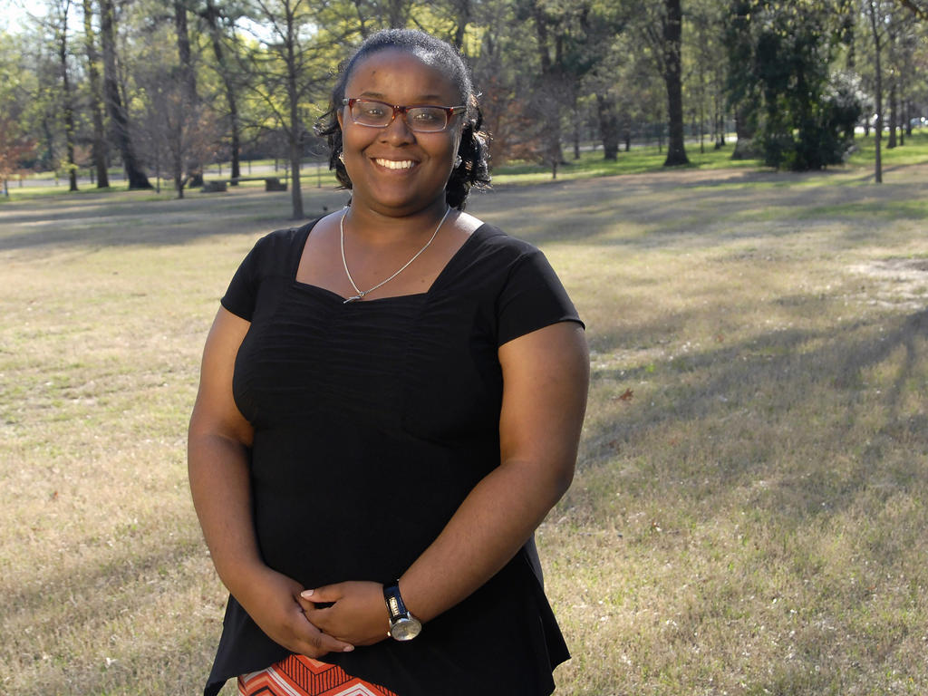 a young African American woman standing near some trees on campus