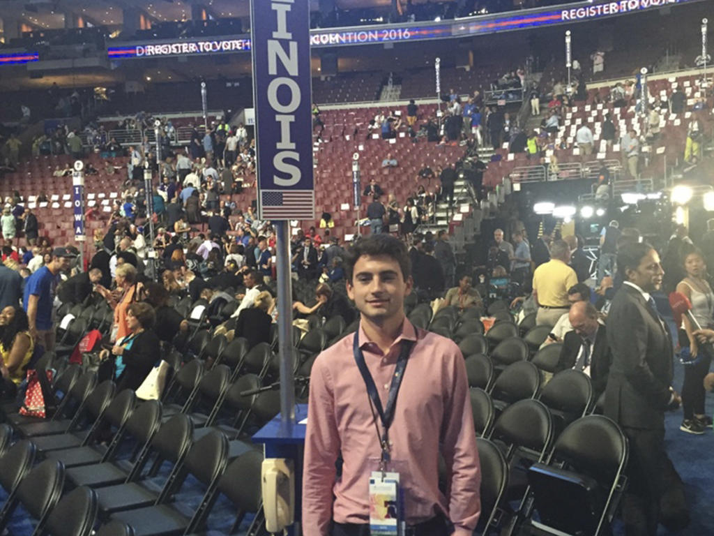 a young man at a political convention taking a picture in front of his seat