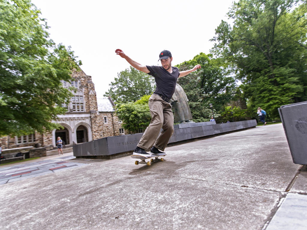 an epic shot of a young man skateboarding new the Diehl statue on Rhodes' campus