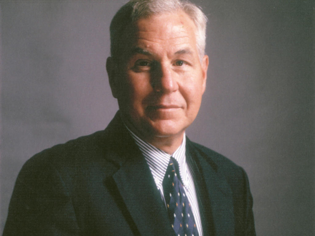 an older white male professor standing in front of a gray background
