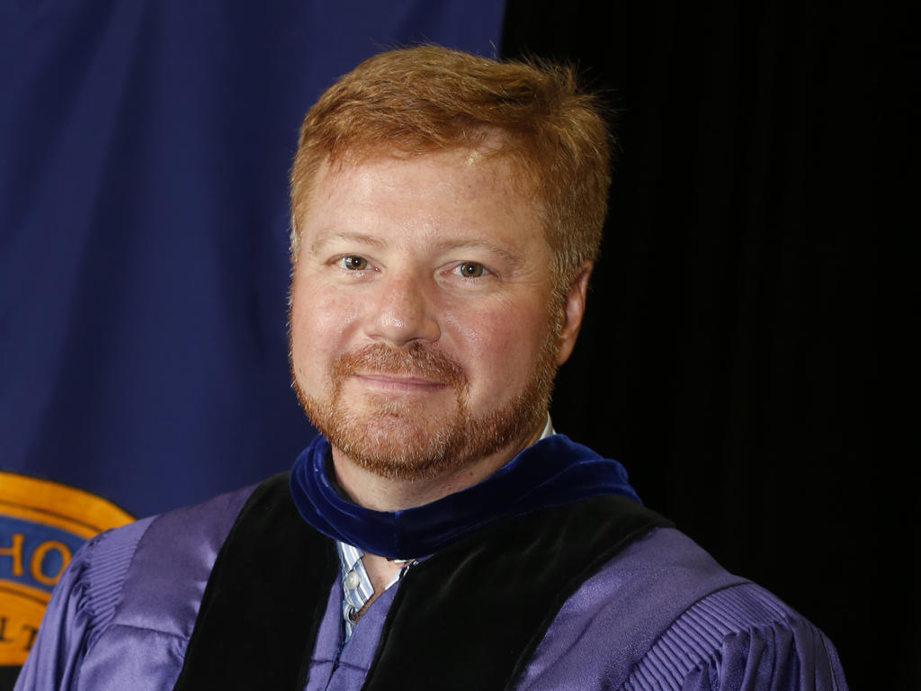 a middle-aged white male professor with red hair standing in his academic robes