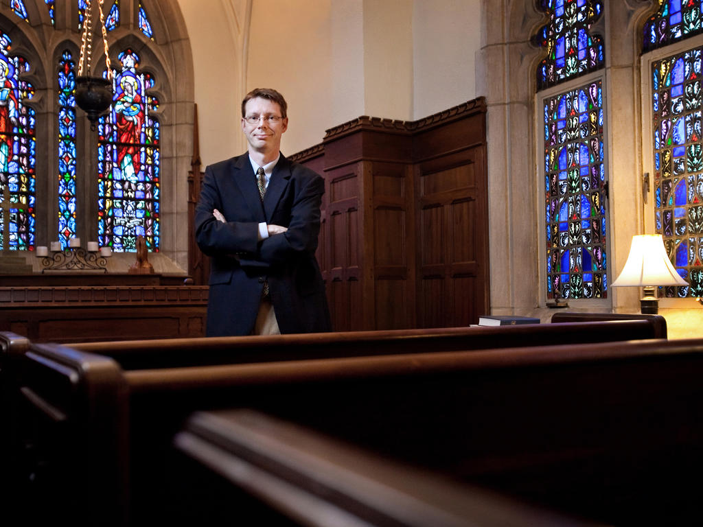 a male professor leaning against a church pew