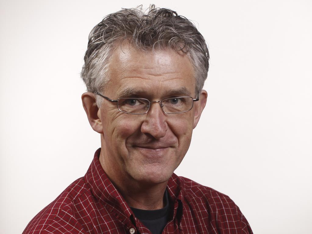 A closeup of an older male professor with square classes and short, curly, gray hair and a red collared shirt