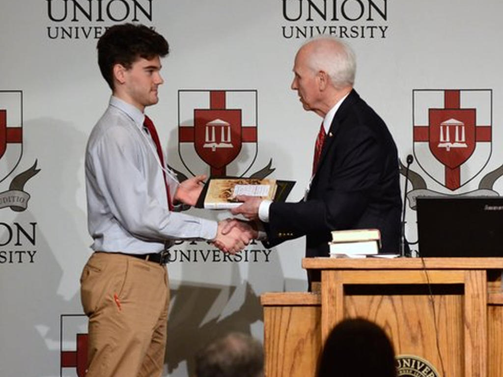 a male student receiving an award from an older male behind the podium
