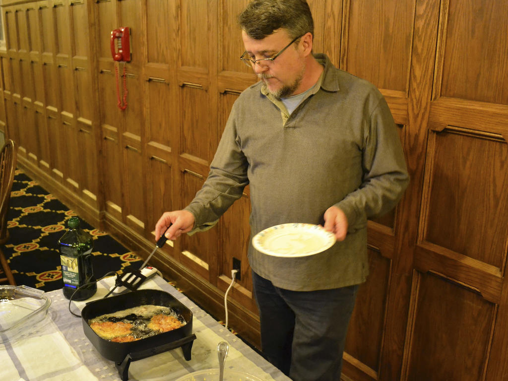 an older white male professor in a dining hall frying food for students