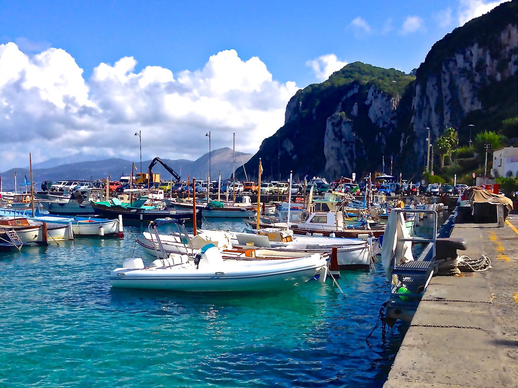 a photo of sailboats in a bright blue-watered harbor peacefully docked near a serene cliff