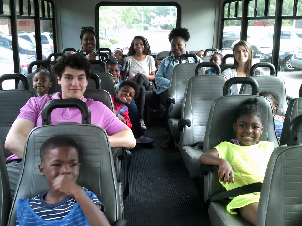 college students seated with pre-K children on a bus