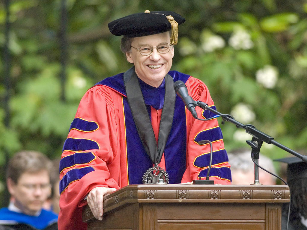 an older white male in academic robes giving a speech on a podium