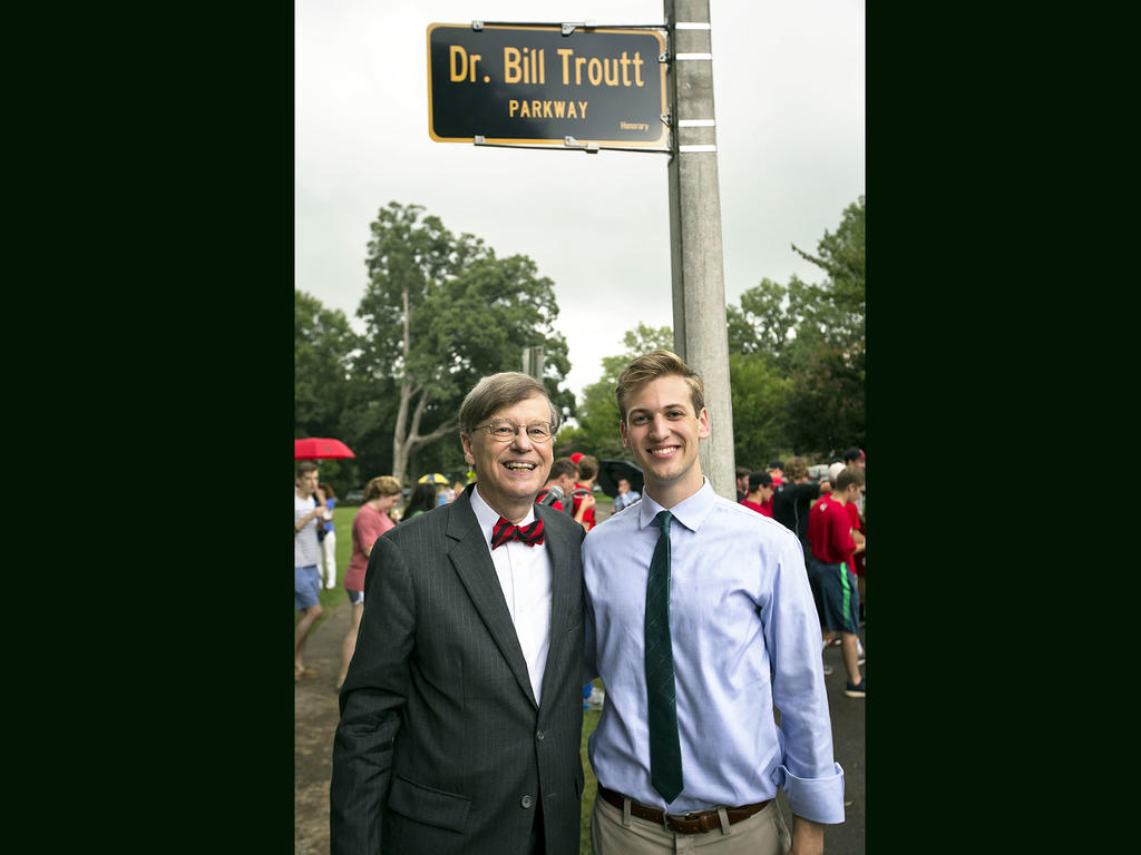 an older man and a young male student standing in front of a street sign