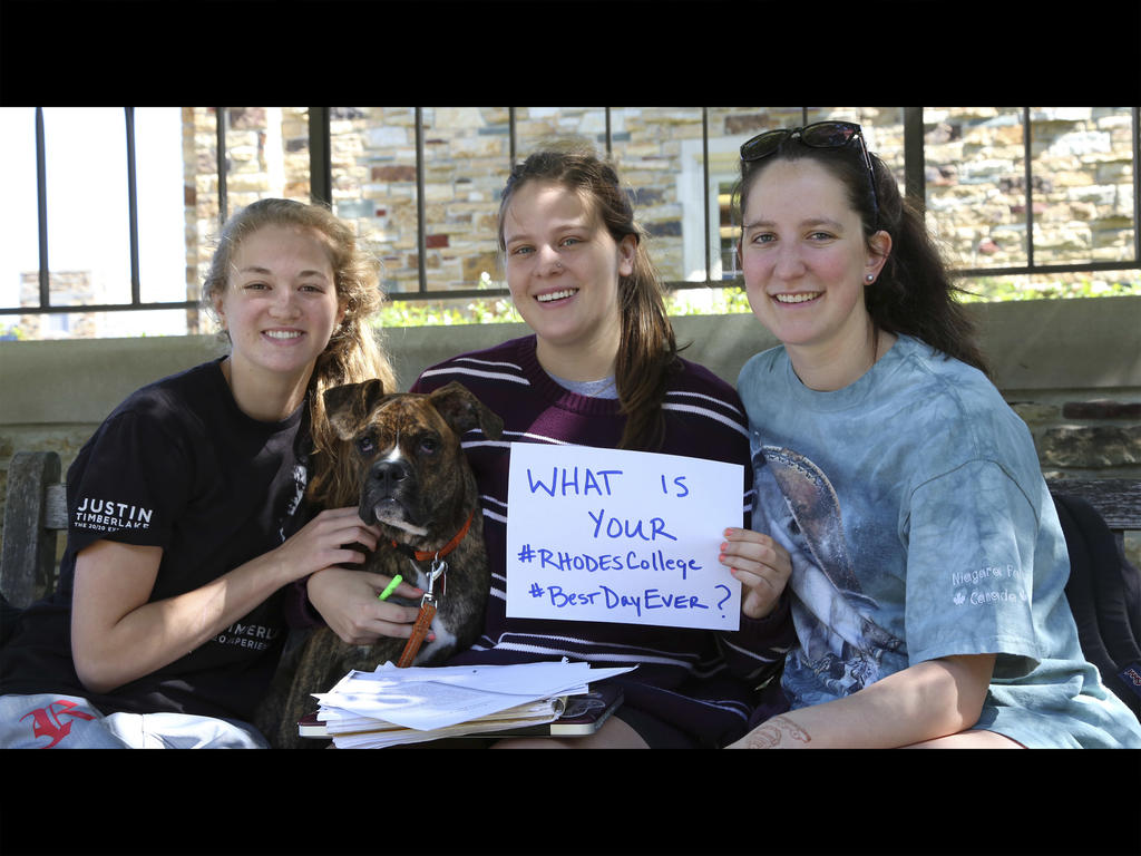 three students holding a paper sign that poses the question "What is your #bestdayever," and one student is holding a dog