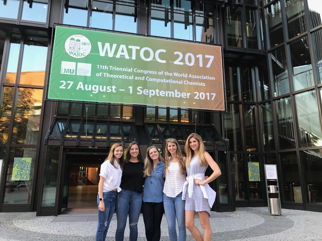 five students standing in front of a building with a sign advertising a chemistry conference