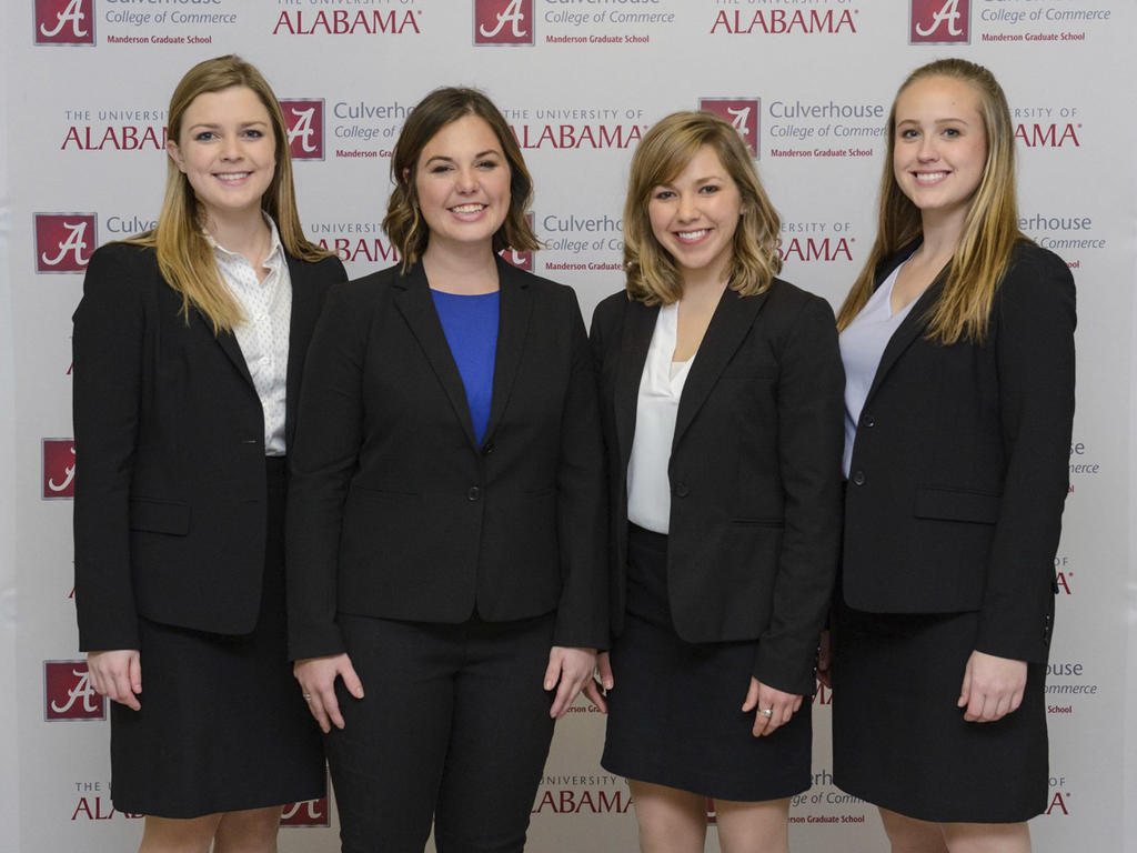 a group of four white women smiling in business attire