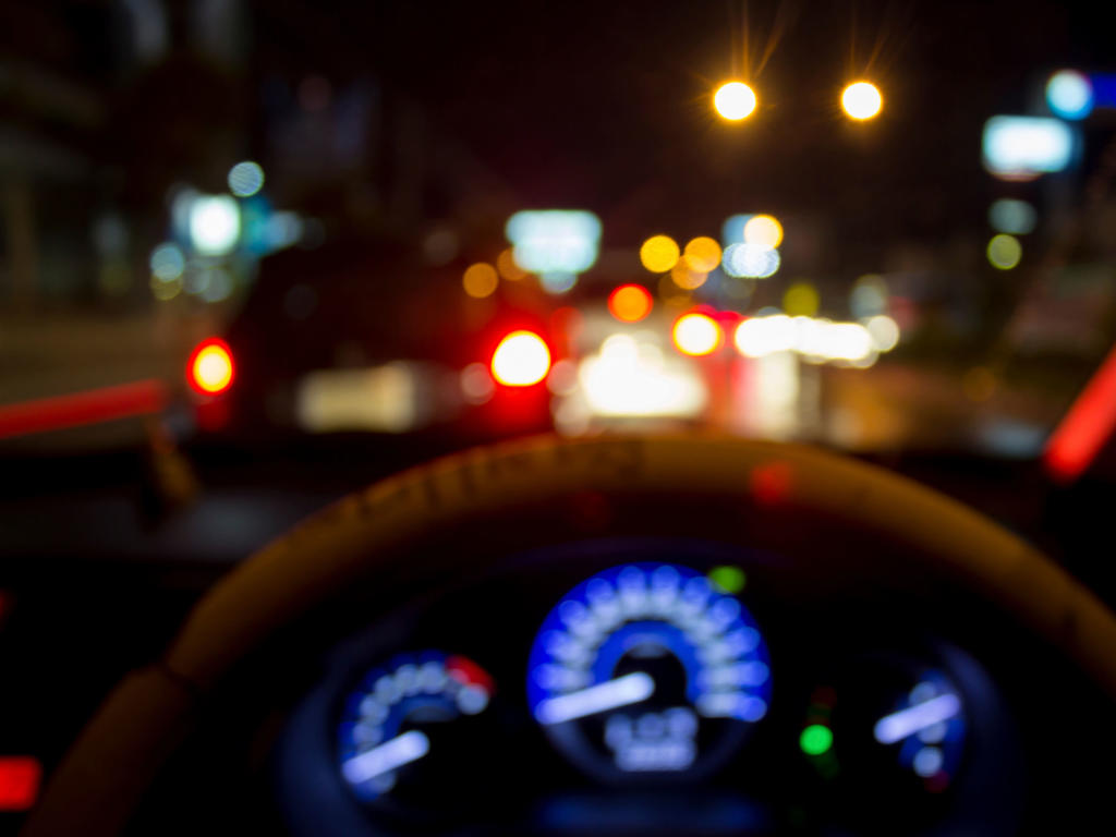 the perspective a driver has when looking at a steering wheel of a car; the gauges and lights of other cars at night