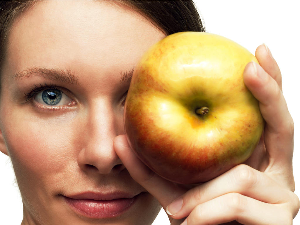 a generic picture of a woman grinning while holding an apple over one of her eyes