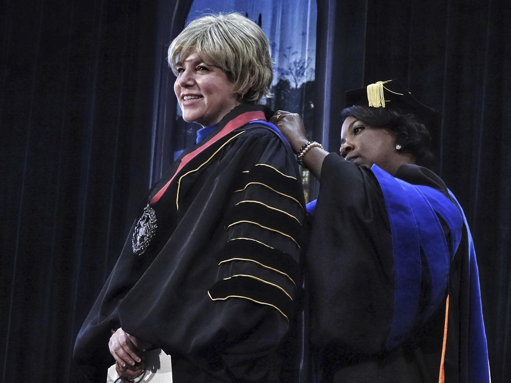 a woman in academic robes receives a medal