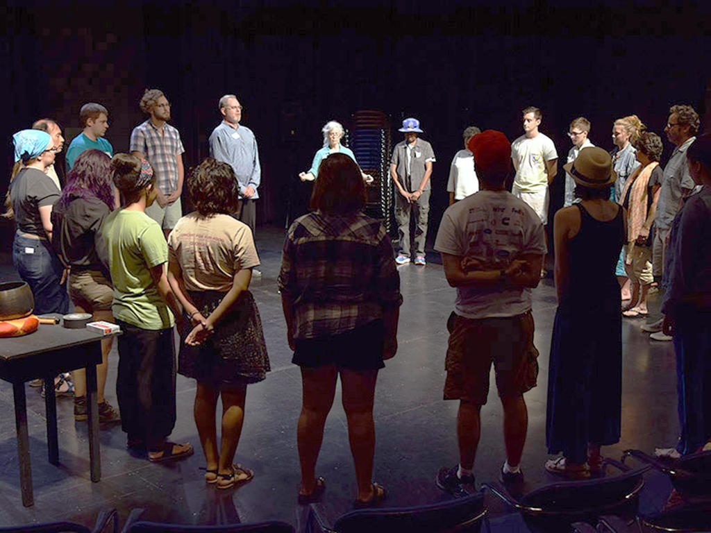 a diverse group of students standing in a circle in the theatre participating in an exercise