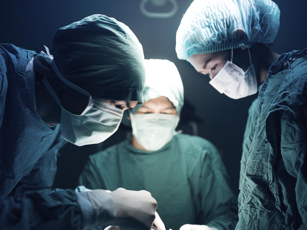 three doctors in scrubs performing surgery