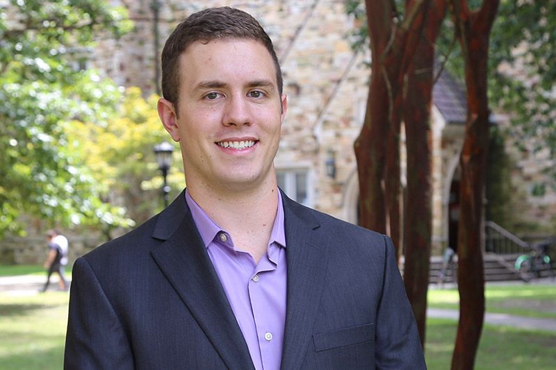 Portrait of Caleb Fowler in front of a Rhodes building surrounded by trees