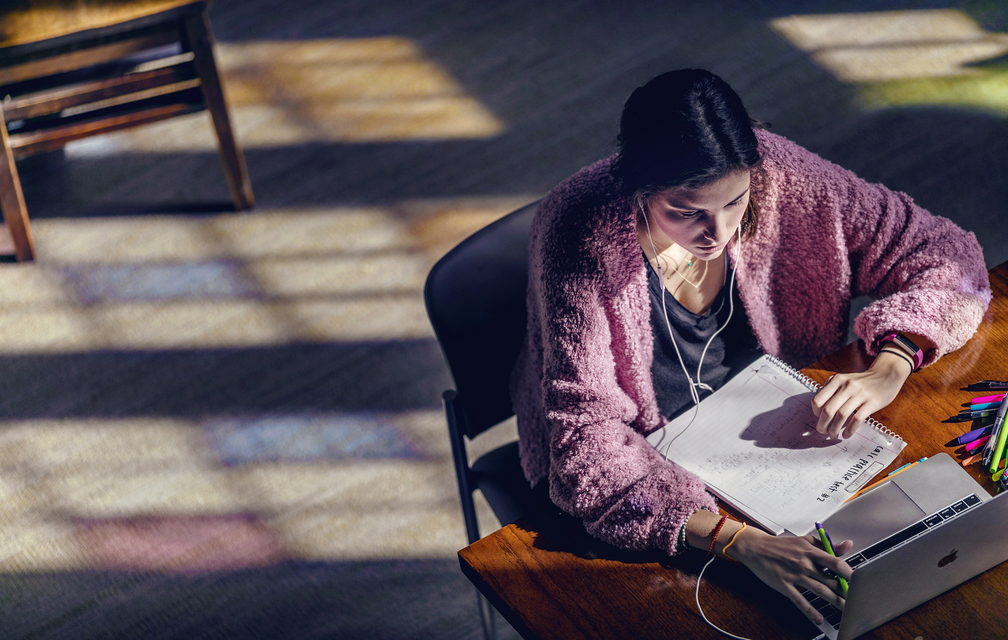 A girl sits in the library reading a paper as the afternoon light streams in from the stained glass windows.