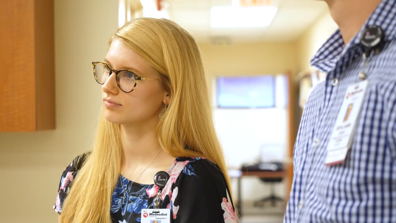An intern wearing her Methodist Hospital name tag stands in a clinic, listening intently.