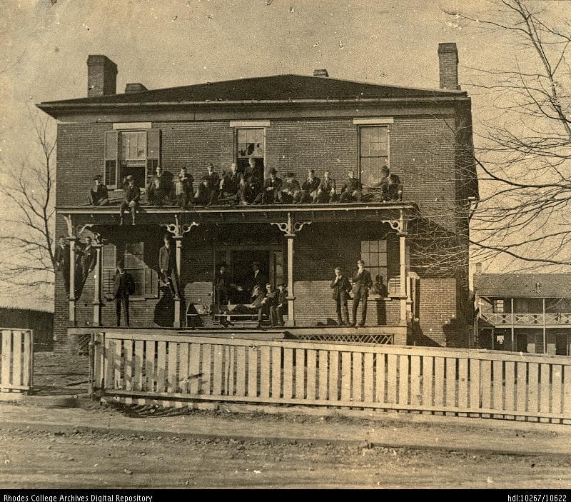 Old photo of students on the porch and top of the portico of a building