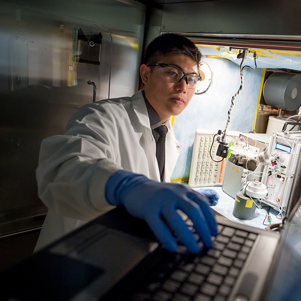 student in lab coat works on a computer