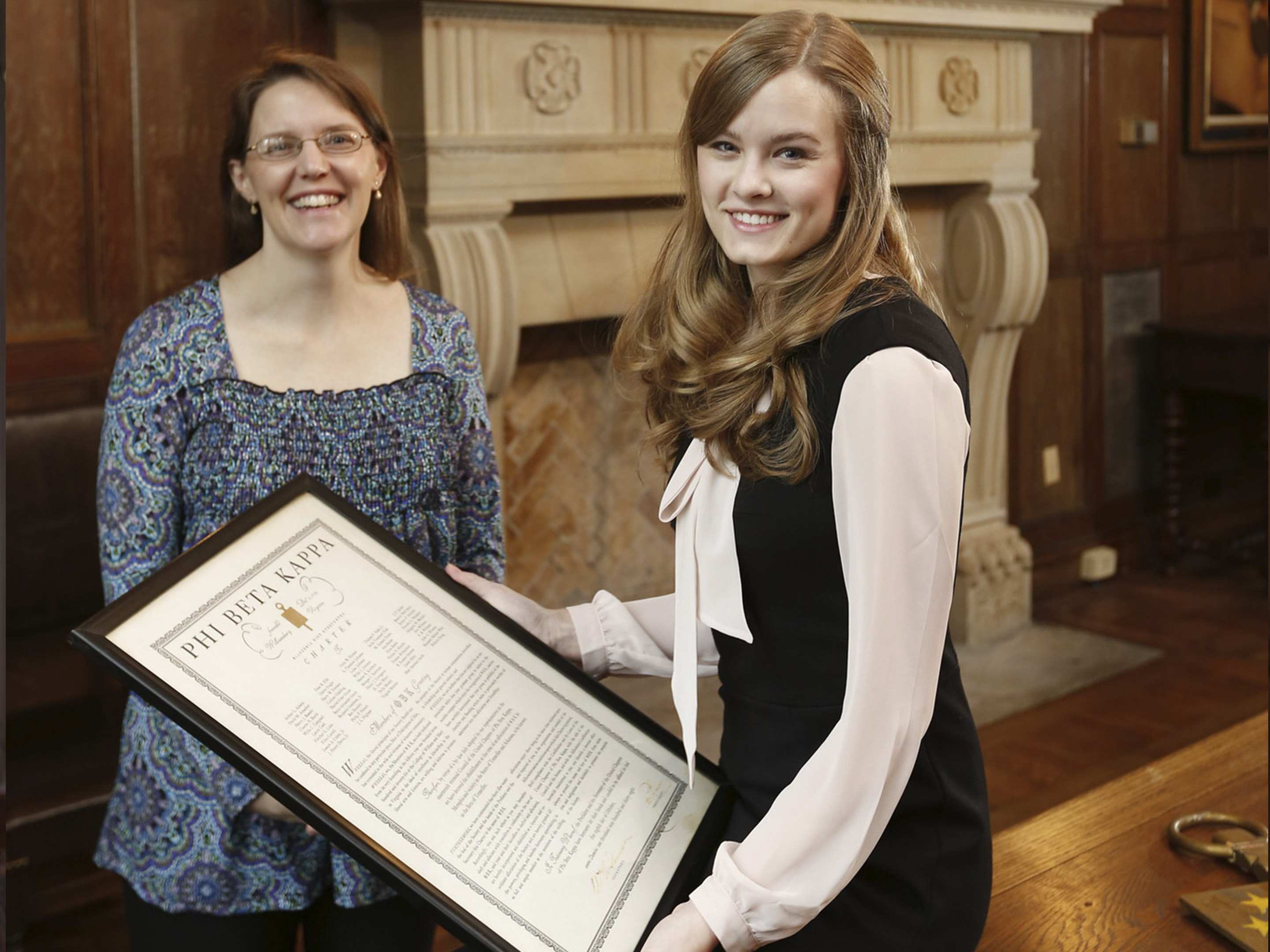 a student holds a Phi Beta Kappa certificate while a professor looks on