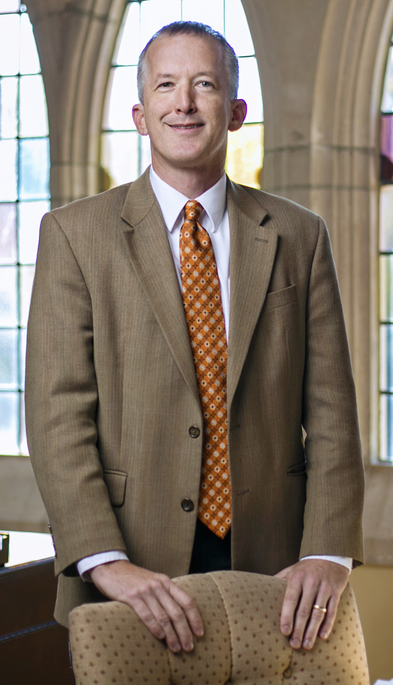 a man stands in front of stained glass windows