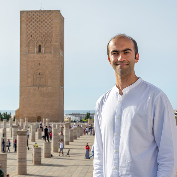 a young man stands in front of a Moroccan tower