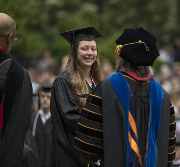 A student in her commencement regalia receives her degree from the president.