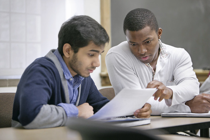 A young man helps a fellow student go over an assignment.