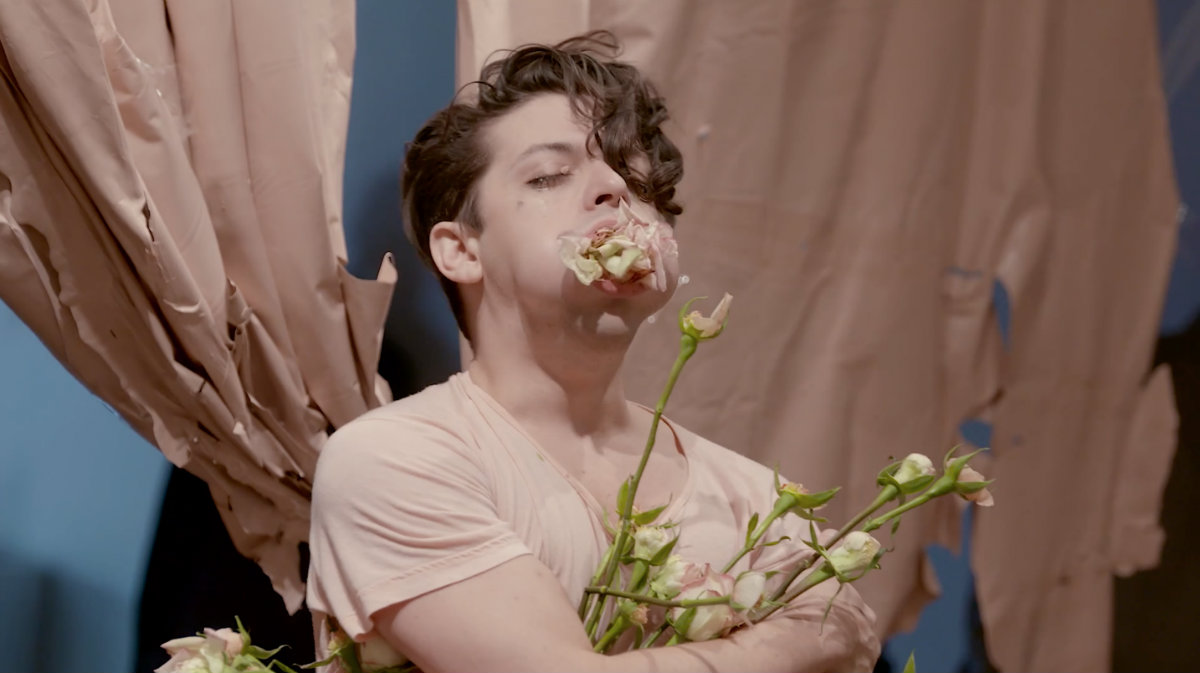 a photo of a male with his eyes closed, holding flowers and with flowers in his mouth