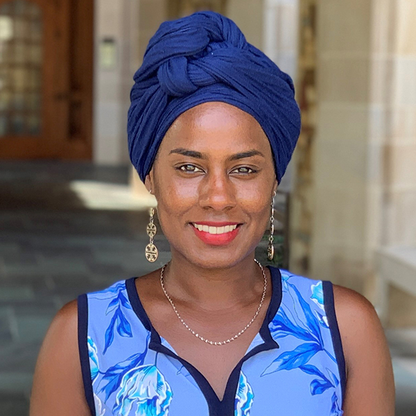 an African American woman in a blue turban and dress smiles at the camera